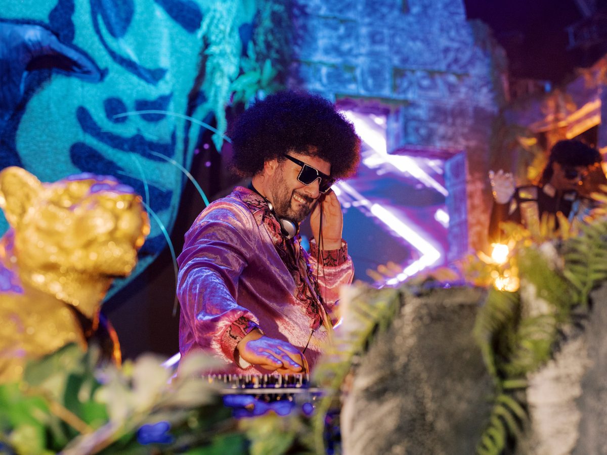 DJ de óculos escuros aos pratos, em cenário néon de selva no evento WILD